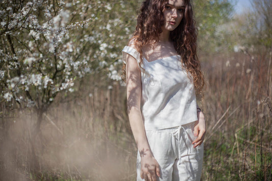 modelka na tle kwitnących drzew w białym komplecie z lnu